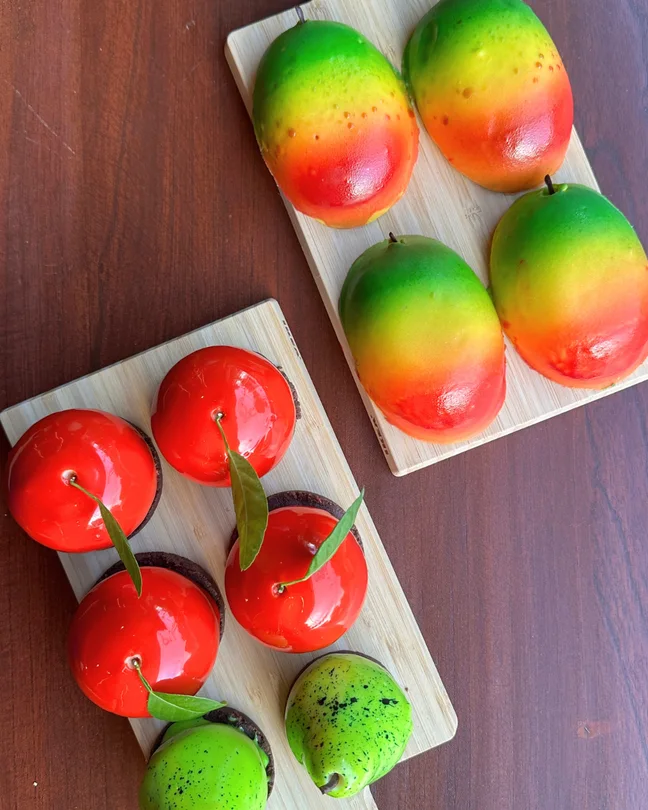Postres decorados con forma de mangos y cerezas sobre una superficie de madera.