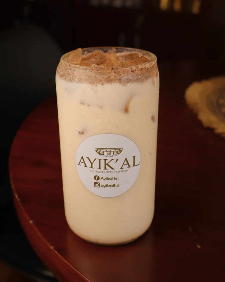 Vaso de bebida cremosa con etiqueta AYIK’AL sobre fondo oscuro.